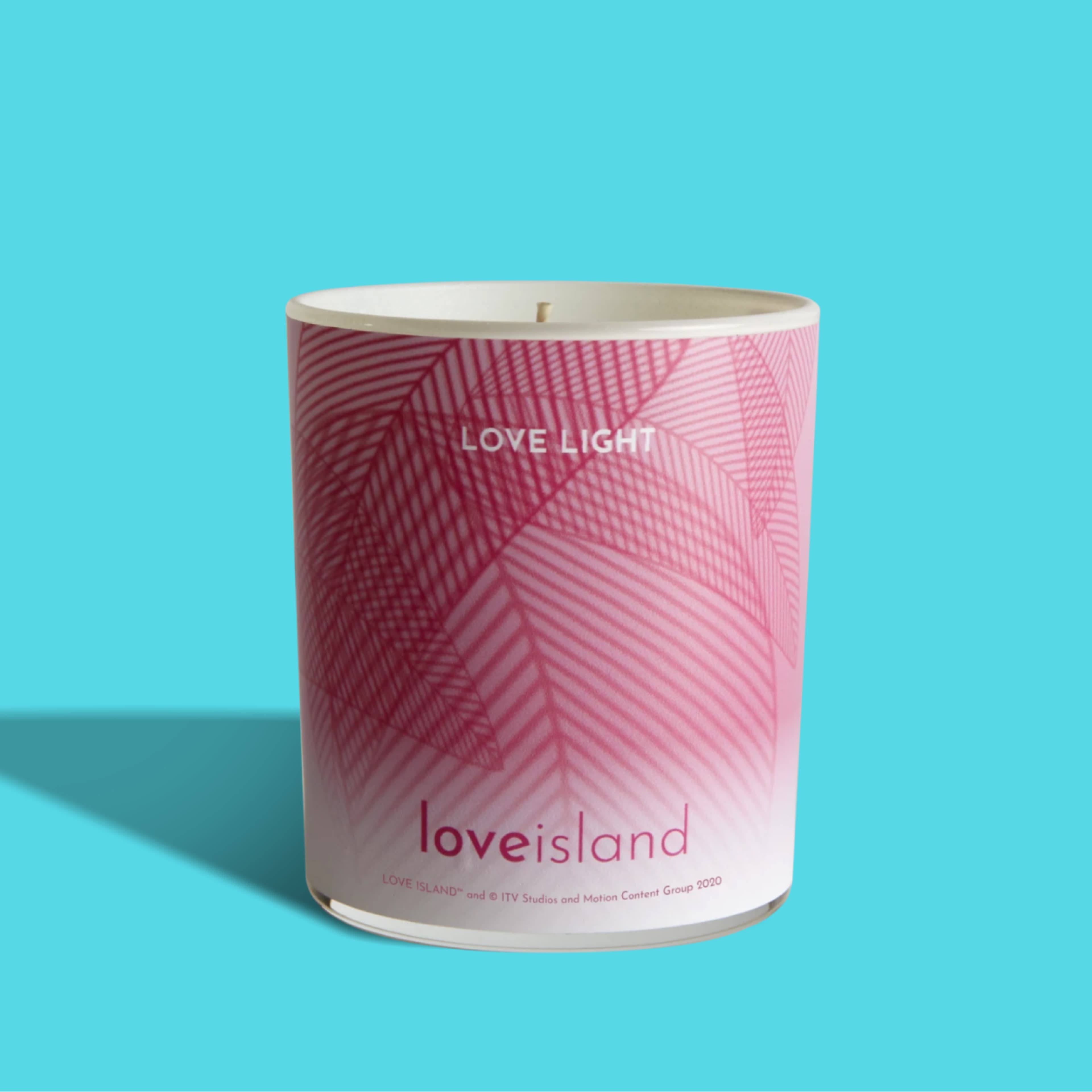 Love Island "Love Light" scented candle in a white tumbler jar with a pink-to-white gradient palm leaf pattern, on a bright turquoise background.