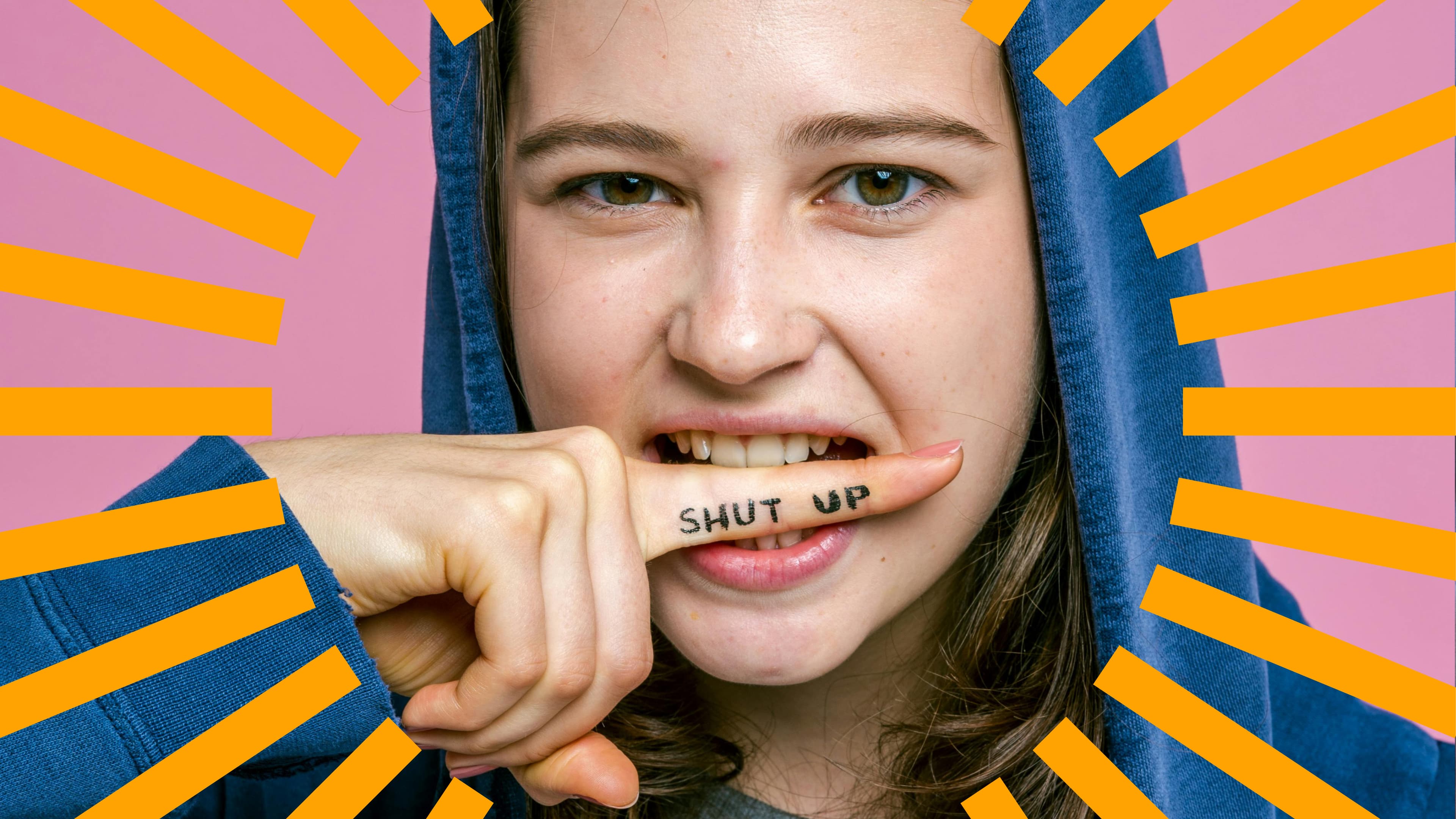 Person in blue hoodie biting finger with 'SHUT UP' written on it, pink background, orange lines radiating outwards.